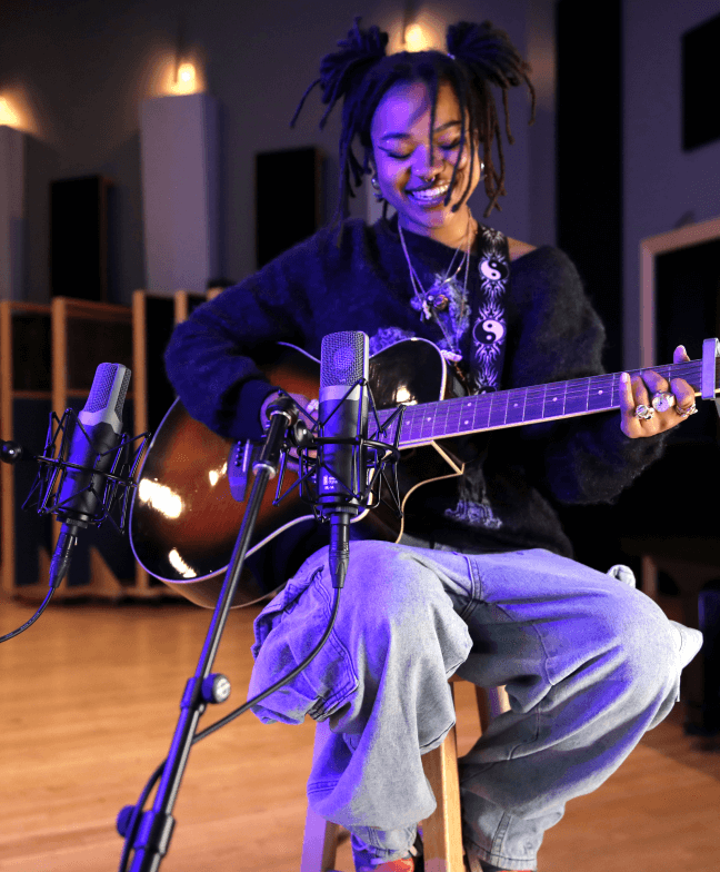 Musician recording acoustic guitar and vocals in a studio using multiple Slate Digital modeling microphones, part of the Virtual Microphone System setup.